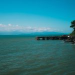 Paisagem costeira de Ilhabela, com um píer diante de águas tranquilas e vegetação tropical exuberante.