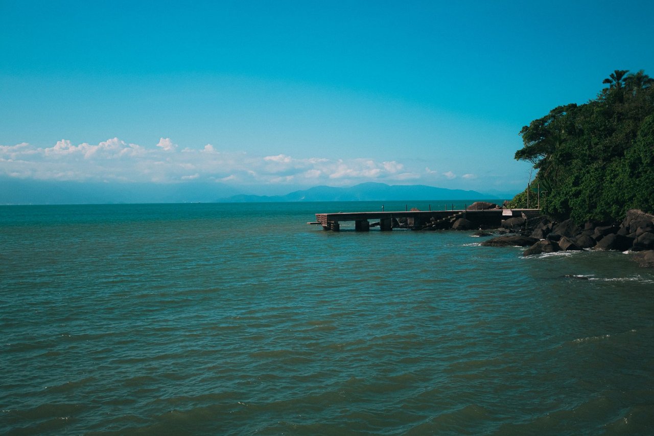 Paisagem costeira de Ilhabela, com um píer diante de águas tranquilas e vegetação tropical exuberante.