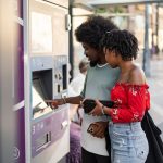 Casal utiliza uma máquina com tela sensível ao toque para comprar passagens em um ponto de ônibus urbano.